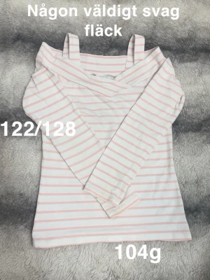 Randig offshoulder topp  - Söt långärmad topp med offshoulder och smala axelband. Vit med ljusrosa ränder. Perfekt för en avslappnad och trendig look.🌸 Svaga fläckar. Storlek 122/128