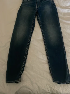 Blå raka jeans med slitningar - Säljer ett par klassiska blå jeans med raka ben och snygga slitningar på framsidan. Jeansen har fem fickor och kontrastsömmar. Perfekta till en avslappnad stil och passar till det mesta i garderoben.