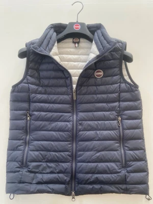 Mörkblå dunväst från Colmar - Snygg mörkblå dunväst från Colmar med quiltad design och två dragkedjeförsedda fickor. Västen har en hög krage och insidan är ljusgrå. Perfekt för lager-på-lager och har Colmar-logga på bröstet. Stängs med dragkedja framtill.