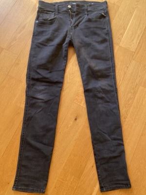 Svarta slim fit jeans från replay - Säljer ett par svarta slim fit jeans från Nudie med klassisk femficksmodell och raka ben. Jeansen har diskreta sömmar och knappgylf. Materialet är mjukt och stretchigt för extra komfort. Perfekta för en avslappnad och stilren look.