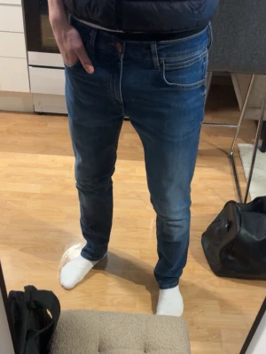 Blå jeans från Wrangler - Snygga blå slim fit/ straight fit jeans från Wrangler med klassisk femficksdesign och subtila slitningar. Jeansen har normal midja, dragkedjegylf och är tillverkade i ett mjukt denimtyg som sitter skönt hela dagen. Perfekta för en avslappnad och trendig look.
