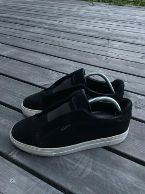 Arigato skor - Stilrena svarta sneakers från Axel Arigato i mocka med diskret logga på sidan. Skorna har vit sula och klassisk låg profil som passar till det mesta. Perfekta för dig som gillar minimalistisk och clean stil.