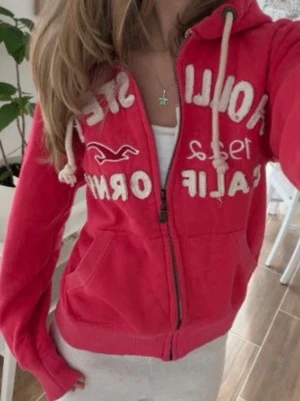 Zip up hoodie Hollister original  - Säljer en zip up hoodie från Hollister med dragkedja, vita broderade detaljer och texten 'Hollister 1922 California' på bröstet. Hoodien har huva med vita snören och två fickor framtill. Perfekt för en avslappnad och cool stil. Har dock ett liten prick men märks inte när man ha på
