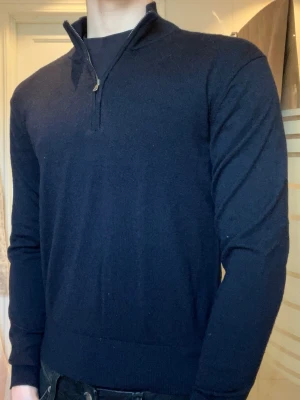 Mörkblå half/quarter zip tröja - Mörkblå stickad tröja av ull, med half-zip och hög krage. Tröjan har långa ärmar och ribbade muddar vid ärmslut och nederkant. Perfekt för lager på lager och enkel att matcha med jeans eller chinos. Tröjan är från uniqlo och storlek XS