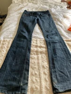 Mörkblå low waisted bootcut jeans  - Säljer ett par snygga blå bootcut jeans från MOTR med dubbla knappar i midjan. Ytterbenslängd: 104cm Innerbenslängd: 83cm Flare: 26cm Midja: 37cm 