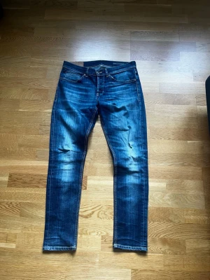 Dondup George Jeans - Snygga blå slim fit jeans med tydliga slitningar och tvättade detaljer på framsidan. Klassisk femficksmodell med dragkedja och knapp i midjan. Jeansen har kontrastsömmar och smal passform som ger en modern look.