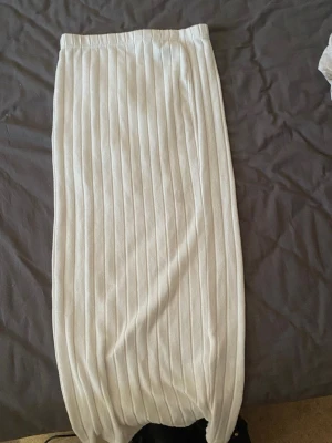 Vit ribbad långkjol från SHEIN - Säljer en vit långkjol från SHEIN i storlek M. Kjolen har ett ribbat mönster och elastisk midja för skön passform. Perfekt att styla med en enkel topp eller stickad tröja för en clean look.