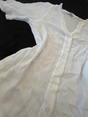 Vit kortärmad blus med knappar - Snygg vit blus med korta ärmar och knappar hela vägen framtill. Blusen har en lätt v-ringad halsringning och är gjord i ett tunt, luftigt tyg som ger en avslappnad känsla. Perfekt att matcha med jeans eller kjol för en fräsch look. Perfekt tills sommaren! Har bundle rabatter! 