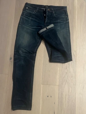 A.P.C. Selvedge - Säljer ett par klassiska blå jeans från A.P.C. modell Petit Standard. Jeansen har rak passform, knappgylf och tydliga kontrastsömmar. Tillverkade i rå denim med snygg tvätt och diskreta slitningar. Perfekta för en clean och stilren look.