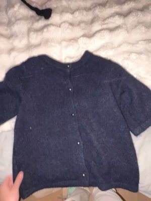 Mörkblå kofta med kort ärm - Mysig mörkblå kofta med korta ärmar och rund halsringning. Koftan har knappar framtill och är tillverkad i ett mjukt, stickat material. Perfekt att slänga över en topp för en avslappnad look.