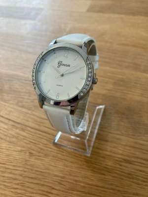 Geneva Quartz Armbandsur med Strass - Säljer en elegant 39mm damklocka. Läder och en boett i vit samt silver. Urtavlan är ljus med minimalistiska markeringar och boetten är prydd med strassdetaljer. Klockan har ett japanskt kvartsurverk, boett i rostfritt stål samt är vattentät. Nyskick enligt bilder. Behöver bara nytt batteri.  Mitt pris: 189 SEK  Skickas alltid snabbt och spårbart. Skriv vid frågor och se gärna mina andra annonser!   GRATIS: För återkommande kunder erbjuder jag personlig experthjälp för dig att göra nya fynd (nytt