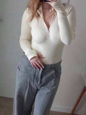 Ribbad beige body med dragkedja - Snygg ribbad body i beige med lång ärm och dragkedja framtill. Kroppsnära passform och mjukt stretchigt material som ger en bekväm känsla. Perfekt att styla med jeans eller kjol för en trendig look.
