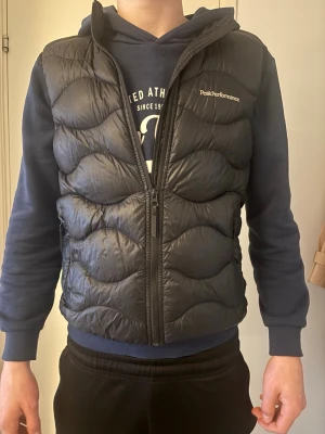 Svart dunväst från Peak Performance - Snygg svart dunväst från Peak Performance. Som ni ser så har den blivit för liten därför jag säljer den, han på bilden är 180 