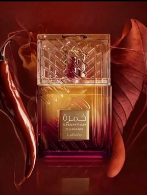 Khamrah Dukhan parfym från Lattafa - Khamrah Dukhan från Lattafa är en exklusiv parfym i en fyrkantig glasflaska med elegant mönstrad kork. Flaskan har en gradient från guld till mörkröd och ger ett lyxigt intryck. Märkets logga och namn syns tydligt på framsidan i guldtext.