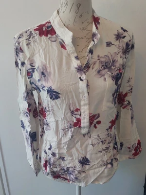 Blommig blus - Blus med vita botten blå/röd/lila blommor. Blus i viskos. Storlek satt som m men är mer en smal.