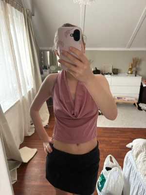 Rosa glittrig halterneck topp - Säljer en rosa glittrig halterneck topp med öppen rygg och draperad front. Toppen är croppad och har en snygg, festlig look med pärldetaljer i nacken. Perfekt för dig som vill sticka ut lite extra.