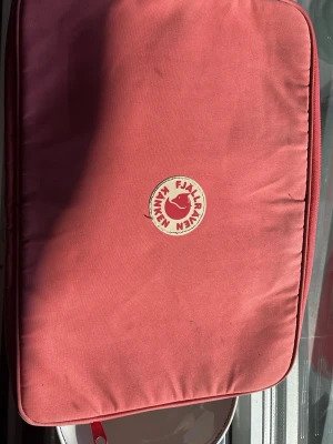 Rosa Kånken datorfodral Fjällräven - Snyggt rosa datorfodral från Fjällräven Kånken med klassisk logga framtill. Tillverkat i slitstarkt tyg med dragkedja och svensk flaggdetalj på sidan. Perfekt för att skydda din laptop i vardagen. Skiiiiiiiit fin färg som är så cool till skolan!!!