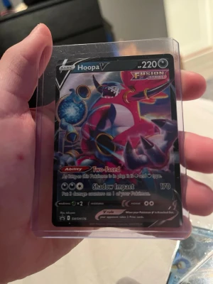 Pokémonkort Hoopa V Fusion Strike - Säljer ett Pokémonkort, Hoopa V från Fusion Strike-serien. Kortet har en färgstark design med lila, rosa och blå toner och är inplastat i ett skyddsfodral. Perfekt för samlare eller Pokémonfans.