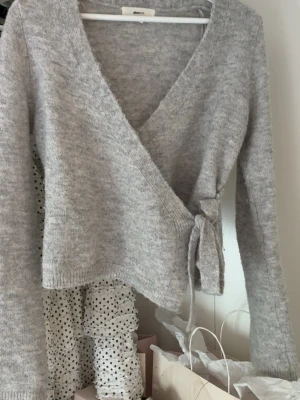 Grå omlottkofta💕 - Mysig grå stickad omlottkofta från gina med knytband i sidan och långa ärmar. Koftan har en mjuk och fluffig känsla, perfekt för lager på lager. Skriv gärna vid frågor!!❣️❣️