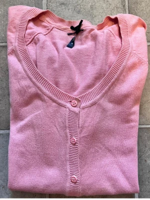 Vår Ljusrosa kofta med knappar - Söt ljusrosa kofta med långa ärmar och knappar framtill. Koftan har ribbade muddar och fickor framtill, perfekt att slänga över en topp för en chill look.