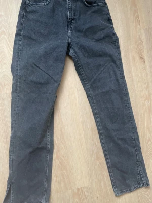 Svarta jeans med slits vid benslut - Säljer ett par svarta jeans med rak passform och cool slits vid benslut. Jeansen har klassiska fickor fram och bak, och är gjorda i denim. Perfekta för dig som vill ha en avslappnad och trendig look.