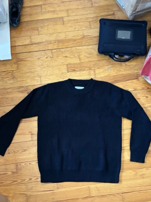 Svart stickad tröja Maison Margiela - Säljer en svart stickad tröja från Maison Margiela. Tröjan har rund halsringning, ribbstickad struktur och långa ärmar. Perfekt för dig som gillar minimalistisk och stilren design. Passar till det mesta och är riktigt skön att bära.