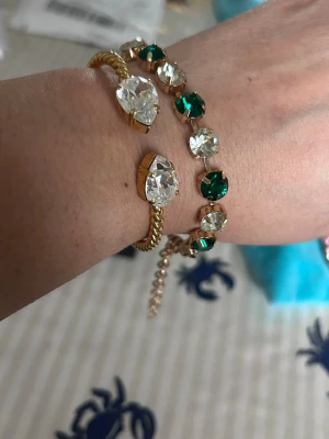 Guldarmband med gröna och klara stenar - Två snygga armband i guldfärg, ett med stora klara stenar i droppform och ett med växelvis gröna och klara runda stenar. Perfekta för att ge din outfit lite extra bling och färg.