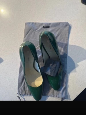 Gröna lackpumps från Miu Miu - Snygga gröna pumps från Miu Miu i glansigt lackmaterial. Klassisk spetsig tå och medelhög klack. Kommer med original dustbag och tillbehör till klacken! Använda två gånger, nypris 12 000kr