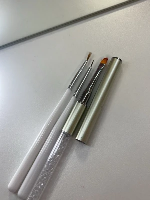 Nagelborstar för nail art - Säljer tre olika nagelborstar perfekta för nail art och detaljerad design. Två borstar har vita handtag och smala borst, medan den tredje har ett silverfärgat handtag med dekorativa kristaller och snedskuren borste. Passar för både gel och akryl. (Nagellack också)