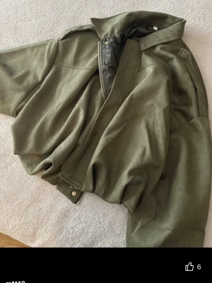 Grön jacka - Snygg olivgrön bomberjacka med klassisk krage och dragkedja framtill. Jackan har en loose passform och är tillverkad i ett mjukt material som känns skönt att bära. Perfekt för dig som vill ha en stilren och trendig jacka till vardags.