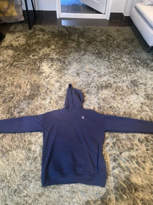 Mörkblå hoodie från Abercrombie & Fitch - Säljer en mörkblå hoodie från Abercrombie & Fitch med klassisk huva och känguruficka framtill. På bröstet finns den ikoniska älg-loggan broderad i vitt. Hoodien är i mjukt bomullsmaterial och har ribbade muddar vid ärmslut och nederkant. Den är aldrig använd då den var för liten och öppna köper hade gått ut 