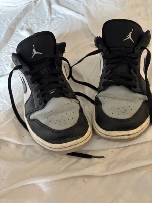 Nike Air Jordan 1 Low svart/vit - Snygga Nike Air Jordan 1 Low sneakers i svart och vitt med klassisk Jumpman-logga på plösen och Swoosh på sidan. Skorna har svart snörning, perforerad tåbox och är tillverkade i läder, låda medföljer ej. Perfekta för dig som gillar streetwear och sportig stil.