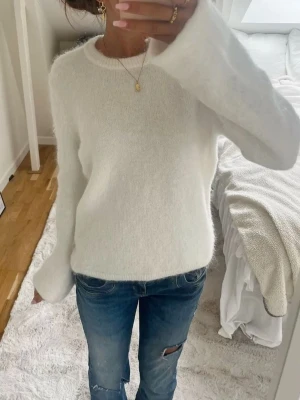 Vit fluffig stickad tröja - Mysig vit stickad tröja med rund hals och långa ärmar. Tröjan har en fluffig och mjuk struktur som ger en avslappnad och trendig look. Perfekt att matcha med jeans för en enkel och stilren outfit.