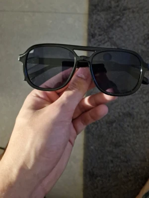 Svarta pilotbågar solglasögon - Snygga solglasögon med svarta pilotbågar och mörka glas. Klassisk aviator-stil med breda skalmar och en cool, tidlös look. Perfekta för att höja stilen på sommaren eller när solen skiner.