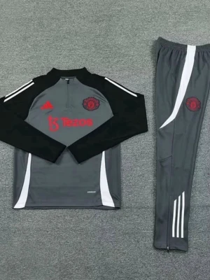 Manchester United träningsset Adidas - Snyggt träningsset från Manchester United och Adidas. Setet är grått med svarta och vita detaljer, röd logga och Tezos-tryck på tröjan. Långärmad tröja med halv dragkedja och matchande byxor med vita ränder. Perfekt för fotbollsträning eller gymmet.