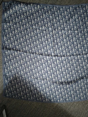 Ny Scarf med mönster - Säljer en snygg blå sjal med ett diskret och tätt mönster i ljusgrått. Sjalen är fyrkantig och har en tunn, mjuk känsla som gör den enkel att styla. Perfekt att slänga över axlarna för en cool look.