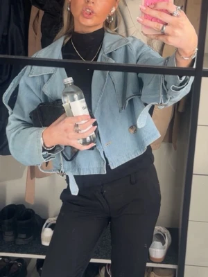 Ljusblå cropped jeansjacka - Cool ljusblå jeansjacka med cropped passform och råa kanter. Jackan har breda slag, en knapp framtill och detaljer som ger en edgy look. Perfekt att slänga över en t-shirt eller hoodie för en avslappnad stil.
