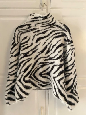 Zebramönstrad stickad polotröja - Säljer en eftertraktad fluffig stickad polotröja från H&M med zebramönster i svart och vitt. Tröjan har oversized passform, långa ärmar och hög krage. Perfekt för dig som vill sticka ut med ett djurmönster i vinter. Materialet känns mjukt och mysigt. Använd endast en gång för provning och säljer pågrund av att det var fel storlek!