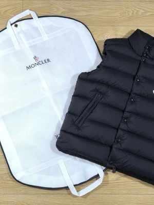 Moncler Tibb - Matte - Stilren svart dunväst från Moncler med hög krage och quiltad design. Västen har två dragkedjefickor framtill och knäppning med knappar. Monclers ikoniska logga sitter på bröstet. Perfekt för lager-på-lager och ger en clean vibe till din outfit.