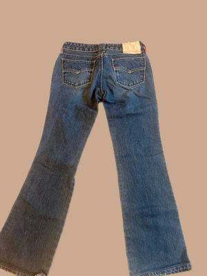 Levi's bootcut,lowwaisted jeans  - Säljer ett par klassiska blå Levi's jeans med bootcut passform och snygga detaljer på bakfickorna. Jeansen har normal midja och är tillverkade i slitstark denim. Perfekta för en avslappnad och trendig look.
