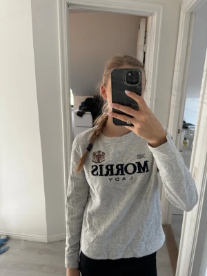 Grå långärmad tröja Morris Lady - Säljer en ljusgrå långärmad tröja från Morris Lady med broderad logga och emblem på bröstet. Tröjan har rund halsringning och är tillverkad i mjukt bomullsmaterial. Xs/s