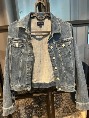 Blå jeansjacka från GANT - Snygg blå jeansjacka från GANT. Väldigt fint skick, syns inte att den är använd! Ganska kort i modellen och rak/figuraydd. Större barnstorlek. 