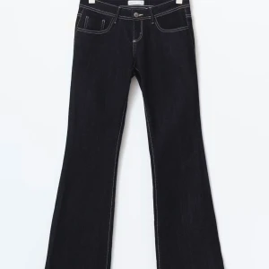 Mörkblå bootcut jeans med kontrastsömmar - Säljer ett par mörkblå bootcut jeans med vita kontrastsömmar och klassisk femficksdesign. Jeansen har låg midja och utsvängda ben för en snygg siluett. Tillverkade i denim med en stilren look som passar till många olika outfits.