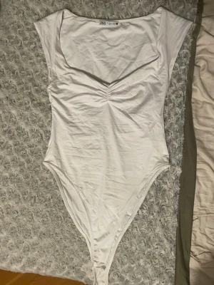 Vit body med v-ringning från Zara - Vit body från Zara i mjukt och stretchigt material. Supersnygg med draperad detalj framtill som ger en bra passform.