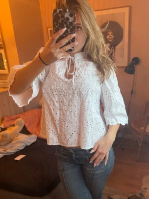 Vit broderad blus med knytning - Superfin vit blus med broderade detaljer och blommönster. Blusen har trekvartsärmar med lätt utsvängd form och knytning vid halsen. Tillverkad i ett luftigt bomullstyg som känns fräscht och somrigt.