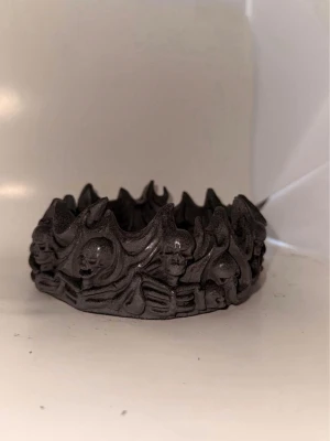 Svart ring med dödskallemönster - Cool ring i svart material med detaljerade dödskallar runt hela bandet och en stor dödskalle inuti. Ringen har en robust och gotisk design, perfekt för dig som gillar alternativa accessoarer.