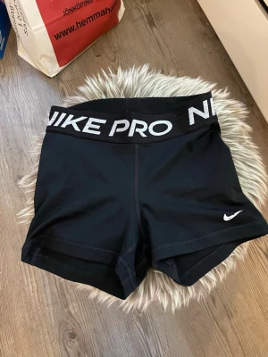 Svarta Nike Pro träningsshorts - Säljer ett par svarta Nike Pro shorts som är i ett riktigt fint skick! Tight passform och korta ben, perfekta för träning. Liten vit Nike-logga på ena benet. Tillverkade i stretchigt syntetmaterial. Shortsen säljs för 175kr då jag behöver bli av med dem så att jag får ny plats i garderoben. OBS! Köparen står för frakt