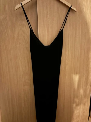 Svart långklänning Gina Tricot - Säljer en svart långklänning från Gina Tricot med tunna axelband och enkel, stilren design. Klänningen har en smal passform och är perfekt för dig som gillar minimalistisk stil. Materialet känns mjukt och följsamt mot kroppen.