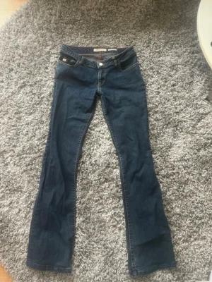 Blå bootcut jeans från miss sixty Jeans - Säljer ett par klassiska blå bootcut jeans från miss sixty Jeans. Jeansen har låg midja, fem fickor och snygga kontrastsömmar. Tillverkade i mjuk denim med lite stretch för extra komfort. Perfekta för en avslappnad och trendig look. Storlek 31