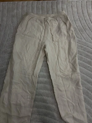 Beiga linnebyxor - Snygga och luftiga beiga linnebyxor med resår och dragsko i midjan. Byxorna har raka ben och är tillverkade i ett tunt, svalt linnematerial. Perfekta för en avslappnad och trendig stil. Lite slitna vid slutet men inget man märker🩷